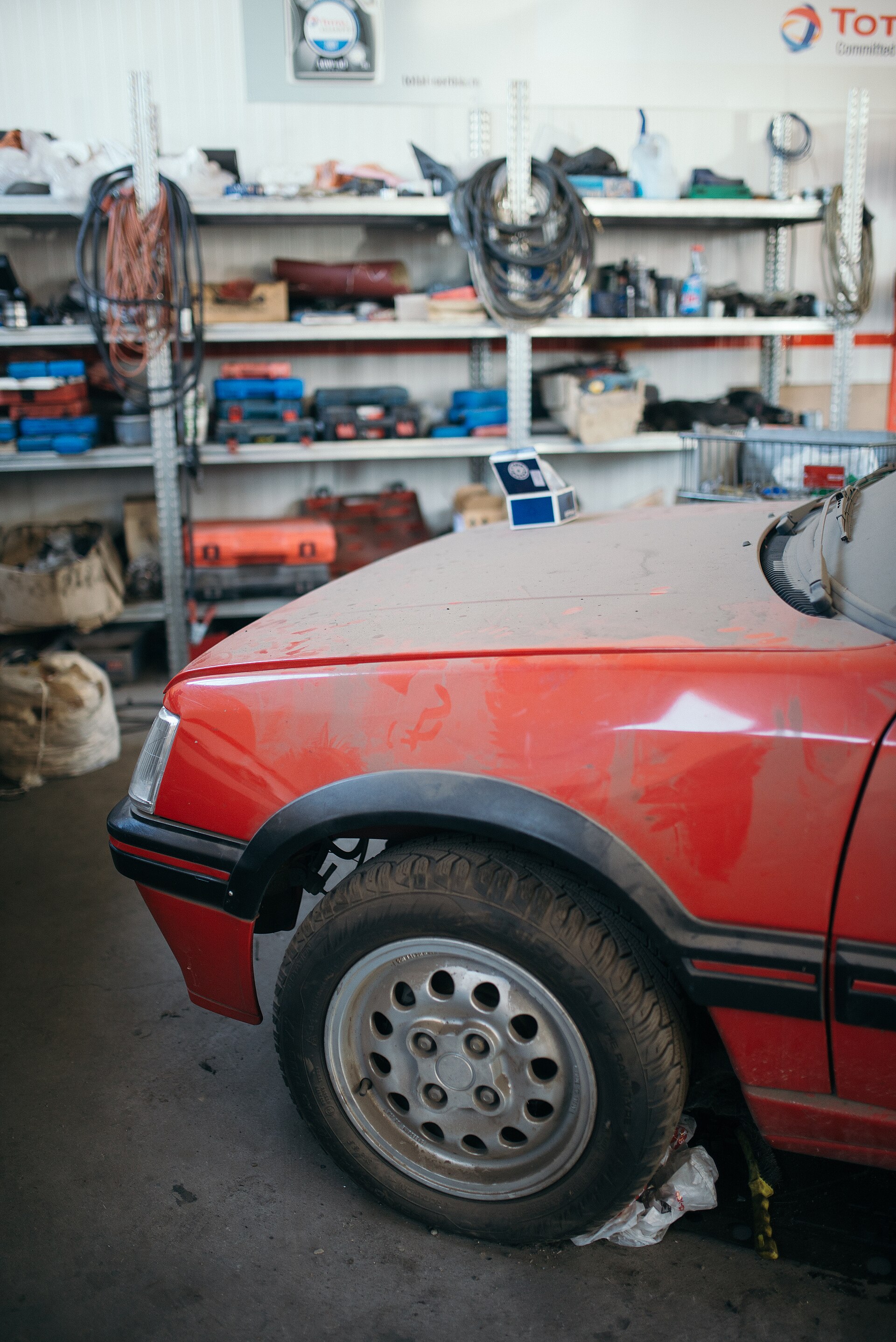 Front corner of a red car parked inside a garage with tool shelves behind it